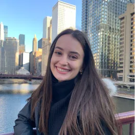 Woman with long brown hair in front of skyscrapers.